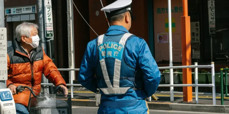 A japanese police officer stands on a crosswalk.